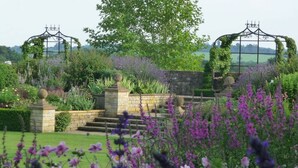 A garden with stone steps, a metal gate, and various plants. - The Crown Hotel (Moreton-in-Marsh)
