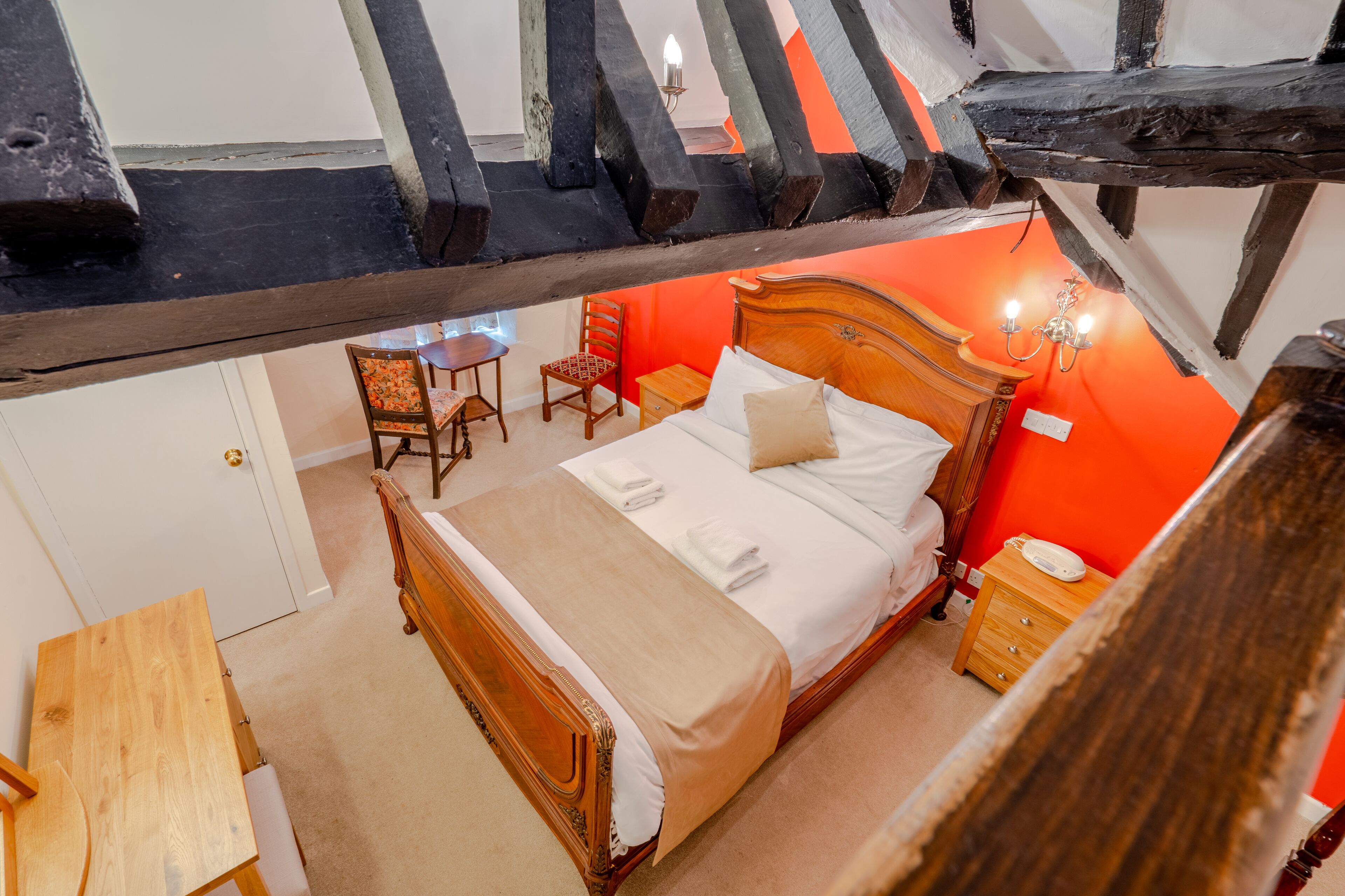 Een slaapkamer met een houten bed, een klein tafeltje, een stoel en een nachtkastje.