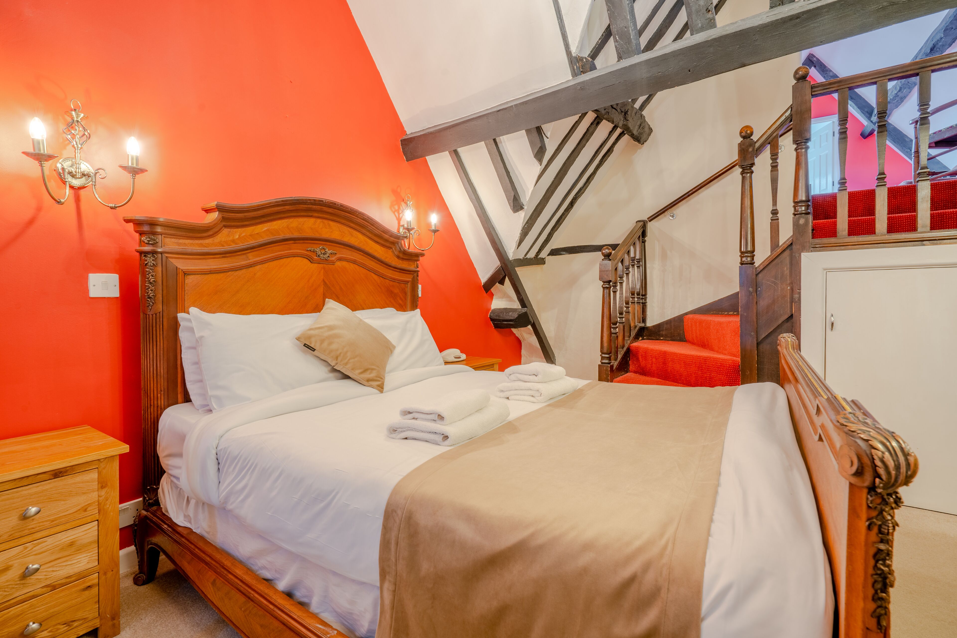 A bed with white linens, a wooden headboard, and a tan throw blanket.