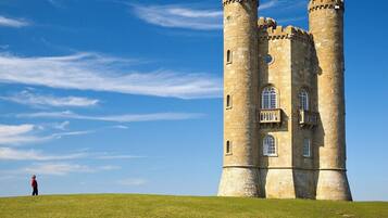 A large stone tower with multiple windows and a balcony, surrounded by a grassy hill under a clear sky.