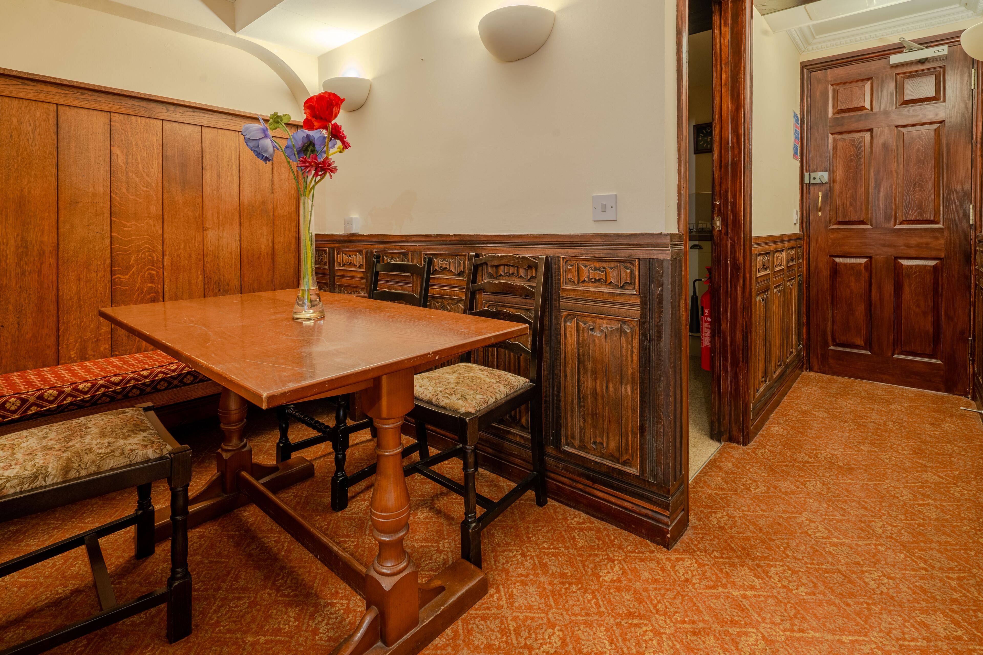 A wooden dining table with a vase of flowers, a bench, and a wooden bench with a cushion.