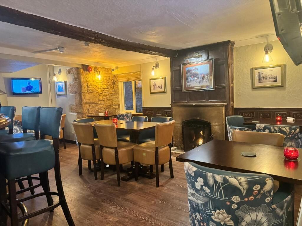 A cozy pub with a stone wall, wooden furniture, a fireplace, and a television screen.