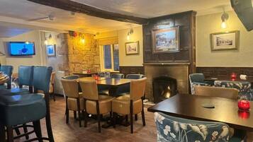 A cozy pub with a stone wall, wooden furniture, a fireplace, and a television screen.