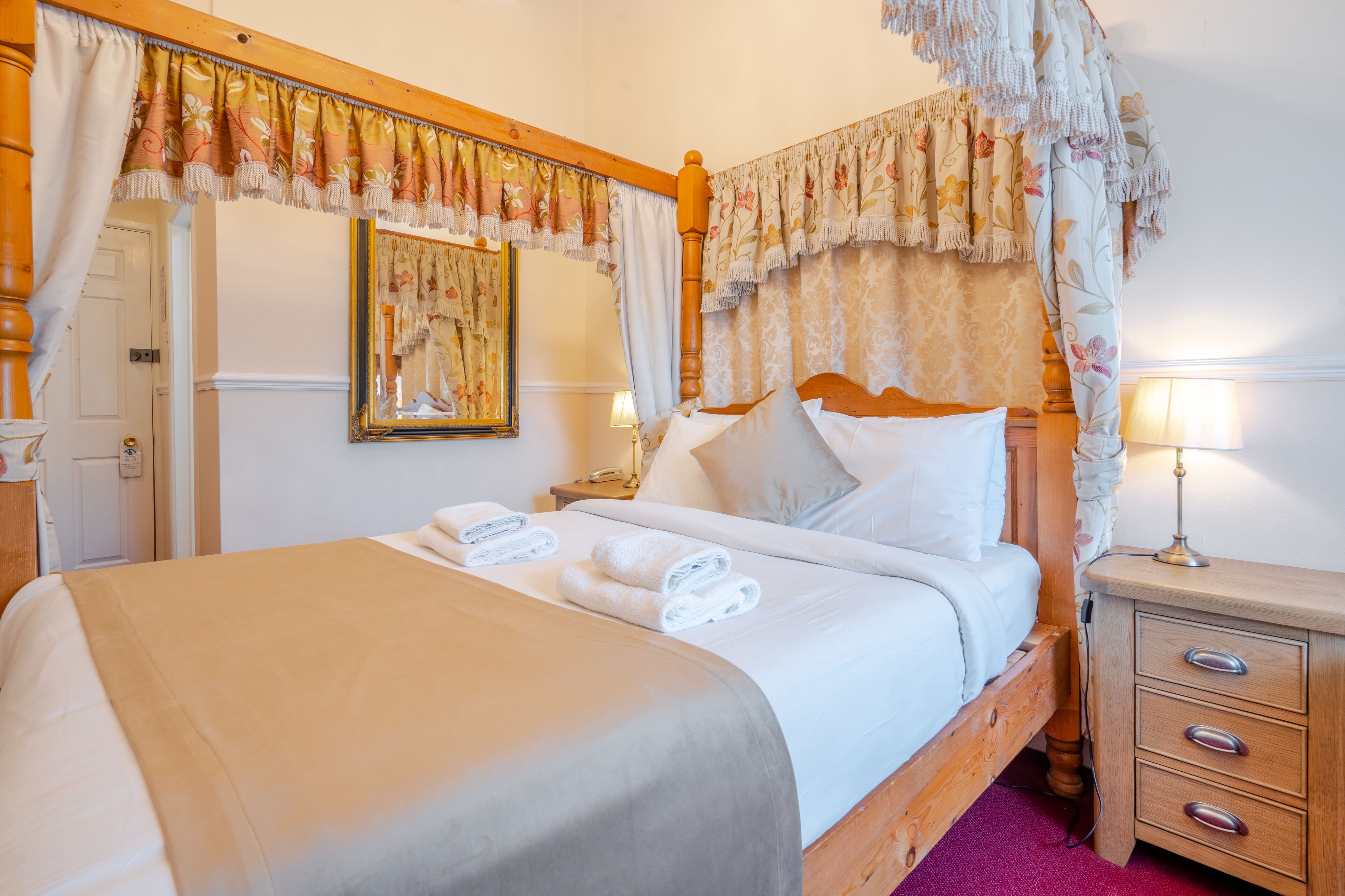 A neatly made bed with white linens and a canopy, a bedside table with a lamp, and a wooden nightstand.