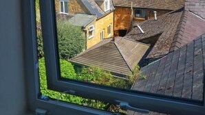 A view through a window of a rural area with stone buildings and a clear blue sky. - The Crown Hotel (Moreton-in-Marsh)