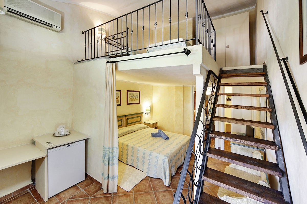 A compact room with a bunk bed, a small desk, and a staircase.