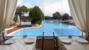 A dining area with a view of a swimming pool and outdoor seating. - Colonna Hotel Du Golf (Olbia)