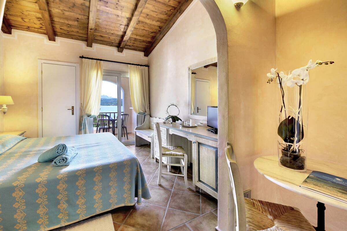 Ein Schlafzimmer mit Bett, Schreibtisch, Stuhl und Blick ins Freie.