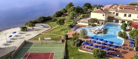 A resort with a swimming pool, beach area, tennis court, and a view of the sea.