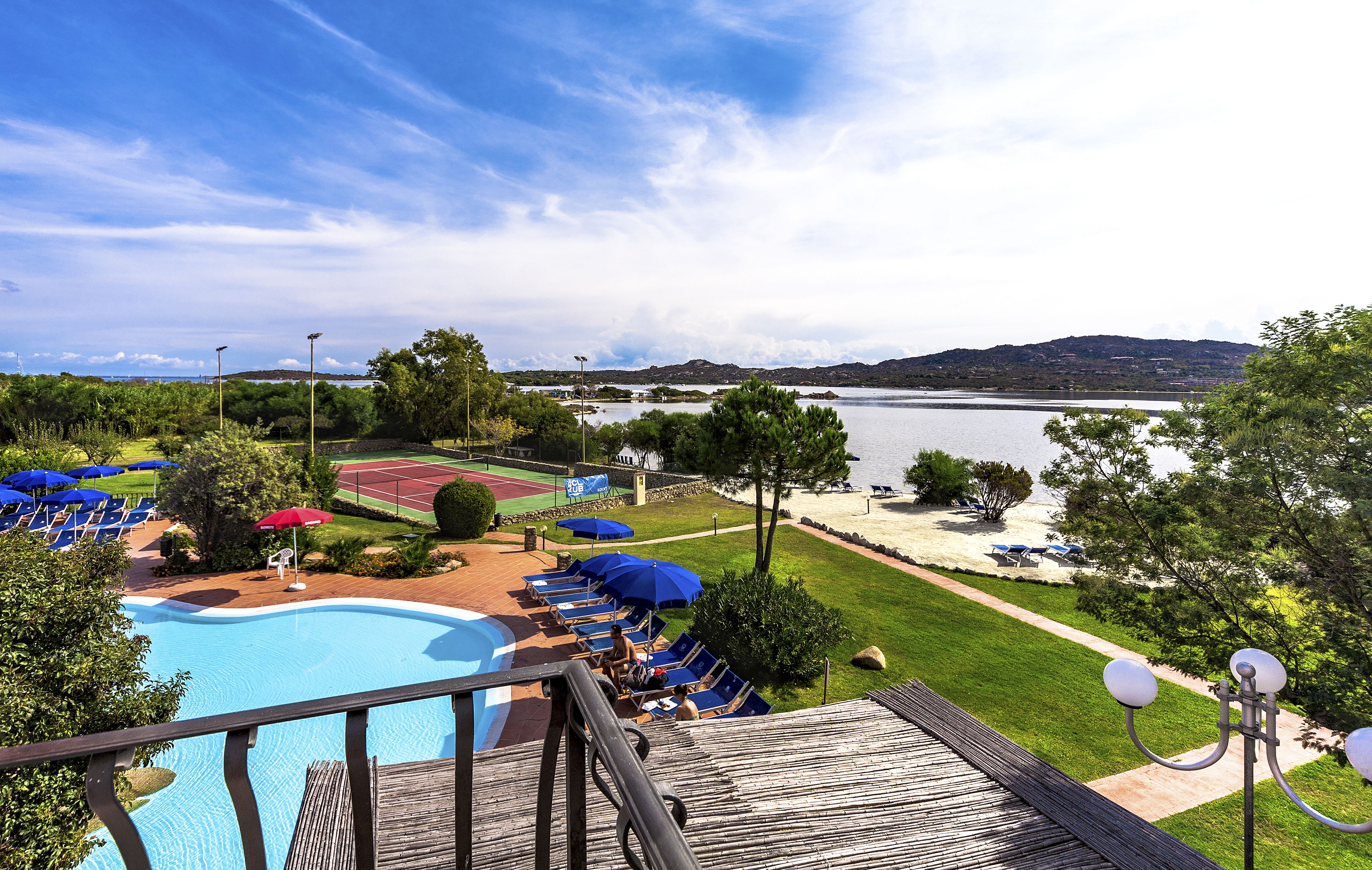 A pool area with lounge chairs and umbrellas, a wooden deck, and a view of a lake and mountains.