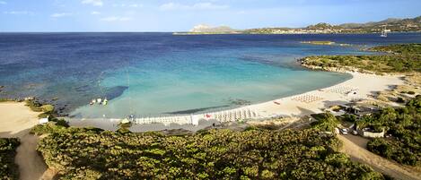 A coastal beach with a clear blue sea, a sandy shore, and a white fence along the beach.