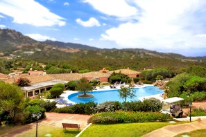 Un complexe hôtelier doté d’une grande piscine, entouré d’une végétation luxuriante et avec des collines en toile de fond.