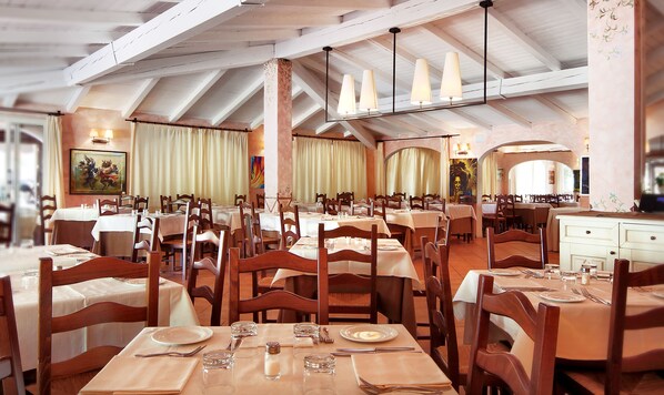 Un restaurante con varias mesas preparadas para comer, sillas de madera y un techo alto con vigas a la vista.