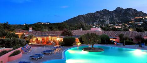 A resort with a swimming pool, lounge chairs, and a mountain backdrop.