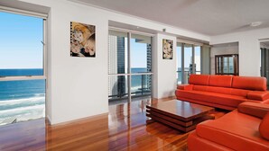 A modern living room with a wooden floor, a red sofa, and a view of the ocean. - Mantra Towers of Chevron (Surfers Paradise)