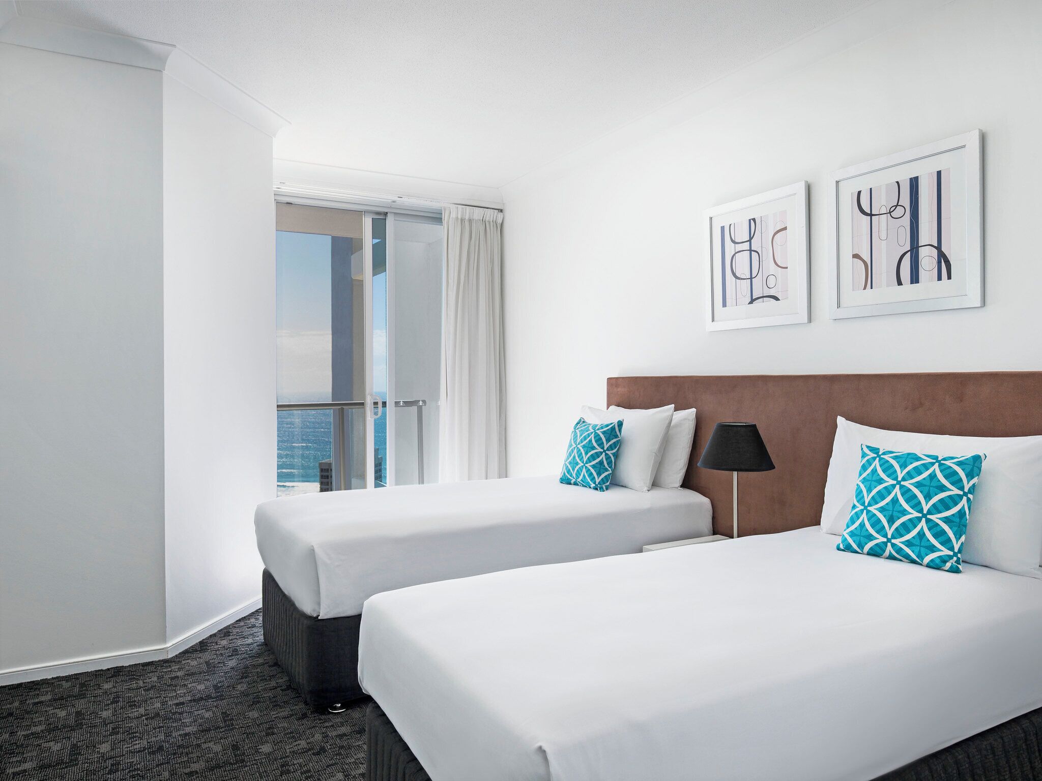 A hotel room with two beds, a view of the city, and artwork on the wall.
