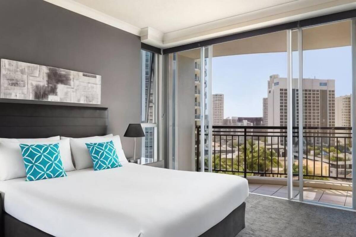A hotel room with a bed, a large window, and a view of buildings.