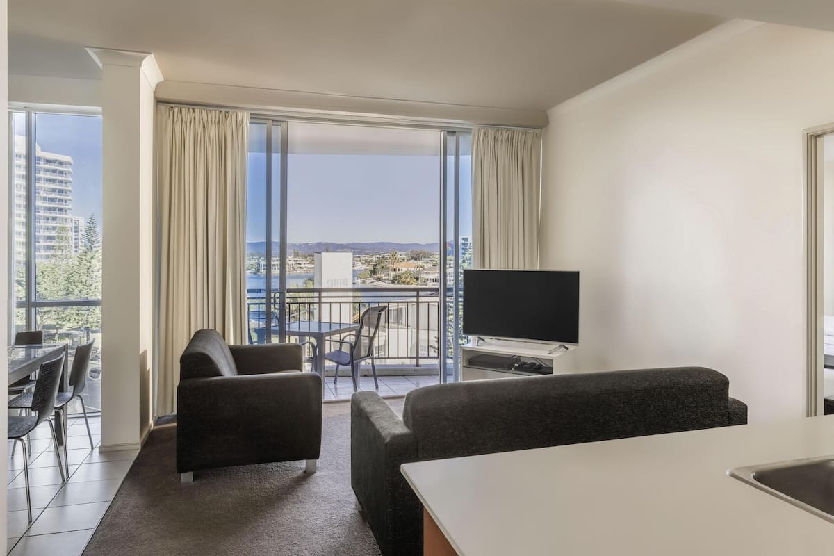 A modern hotel room with a balcony, a flat-screen TV, a dining area, and a sofa.