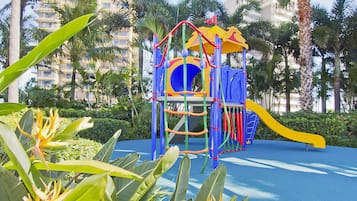 Kids can play and climb in this vibrant playground surrounded by lush greenery and palm trees.