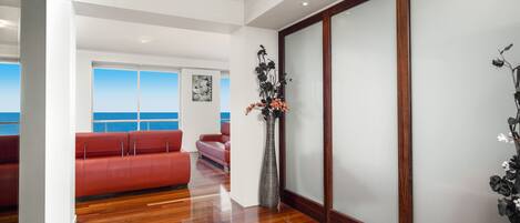 Un interior moderno con suelo de madera, asientos rojos, un florero con flores y vista al mar.