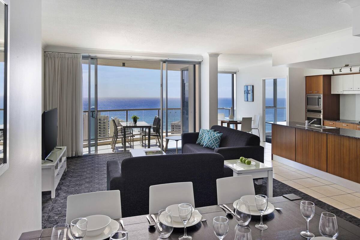 A modern hotel room with a balcony, a dining area, and a kitchen.