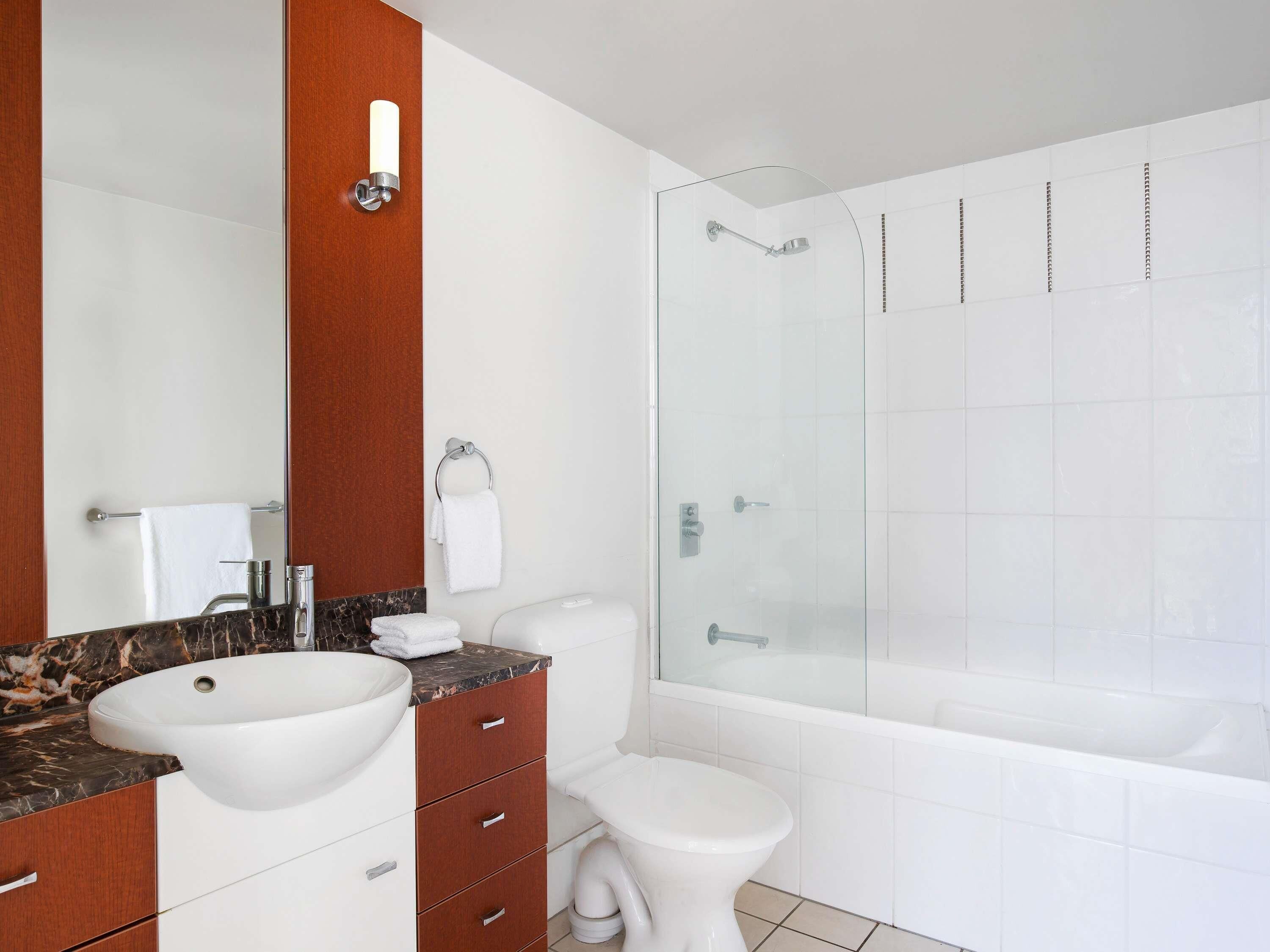 A modern bathroom with a large mirror, a marble countertop sink, a toilet, and a glass-enclosed shower.