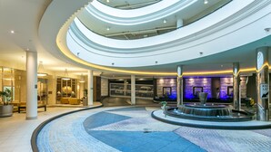 A multi-level atrium with a central water feature, glass railings, and a stone wall with a clock. - Mantra Towers of Chevron (Surfers Paradise)