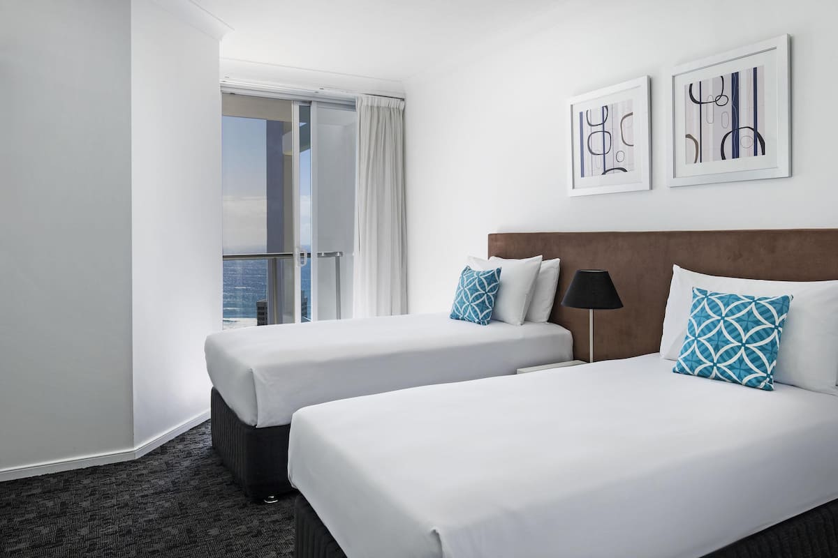 A hotel room with two beds, a view of the city, and artwork on the wall.