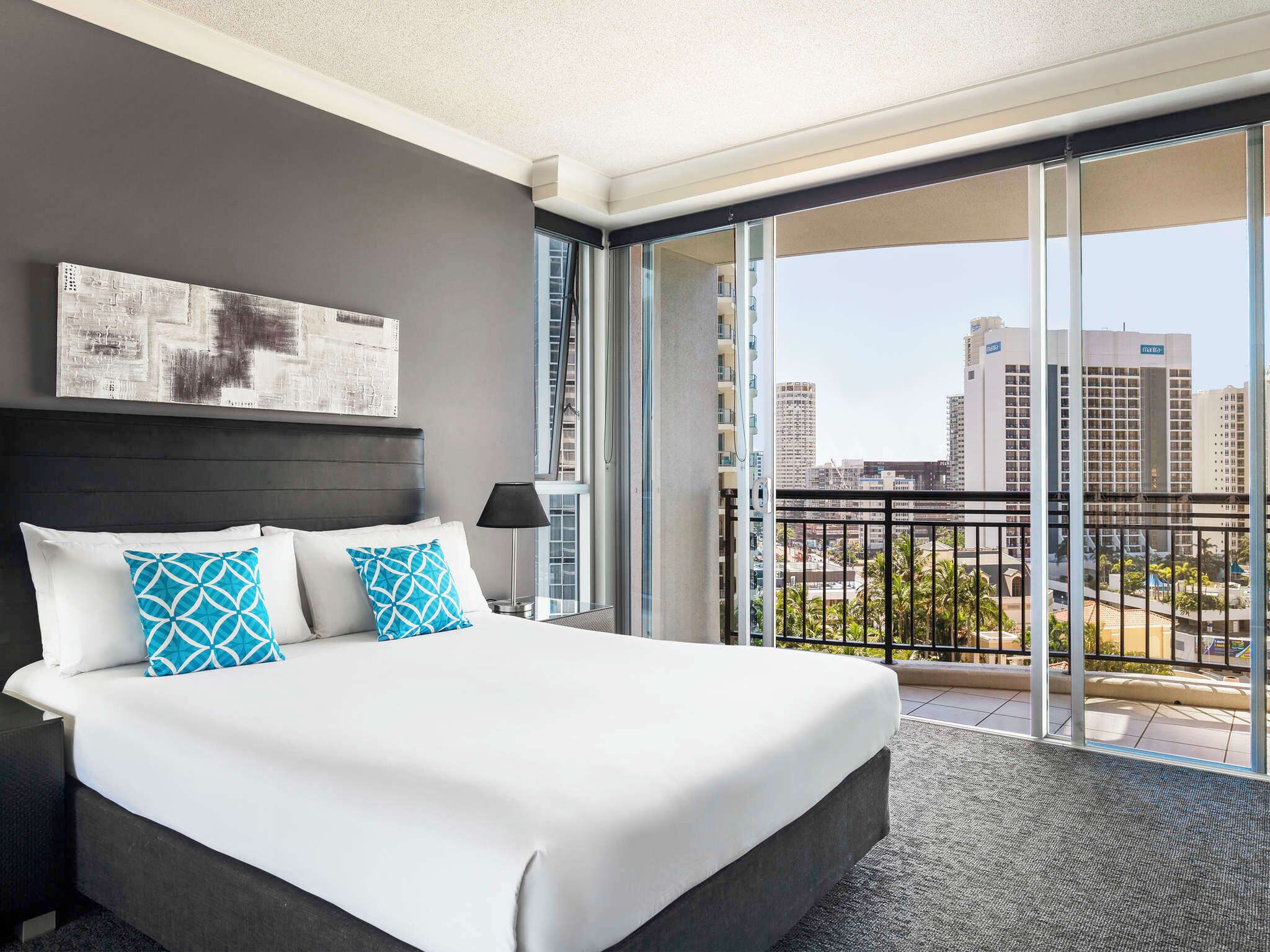 Una habitación de hotel moderna con una cama grande, un balcón con vistas a la ciudad y un cuadro en la pared.