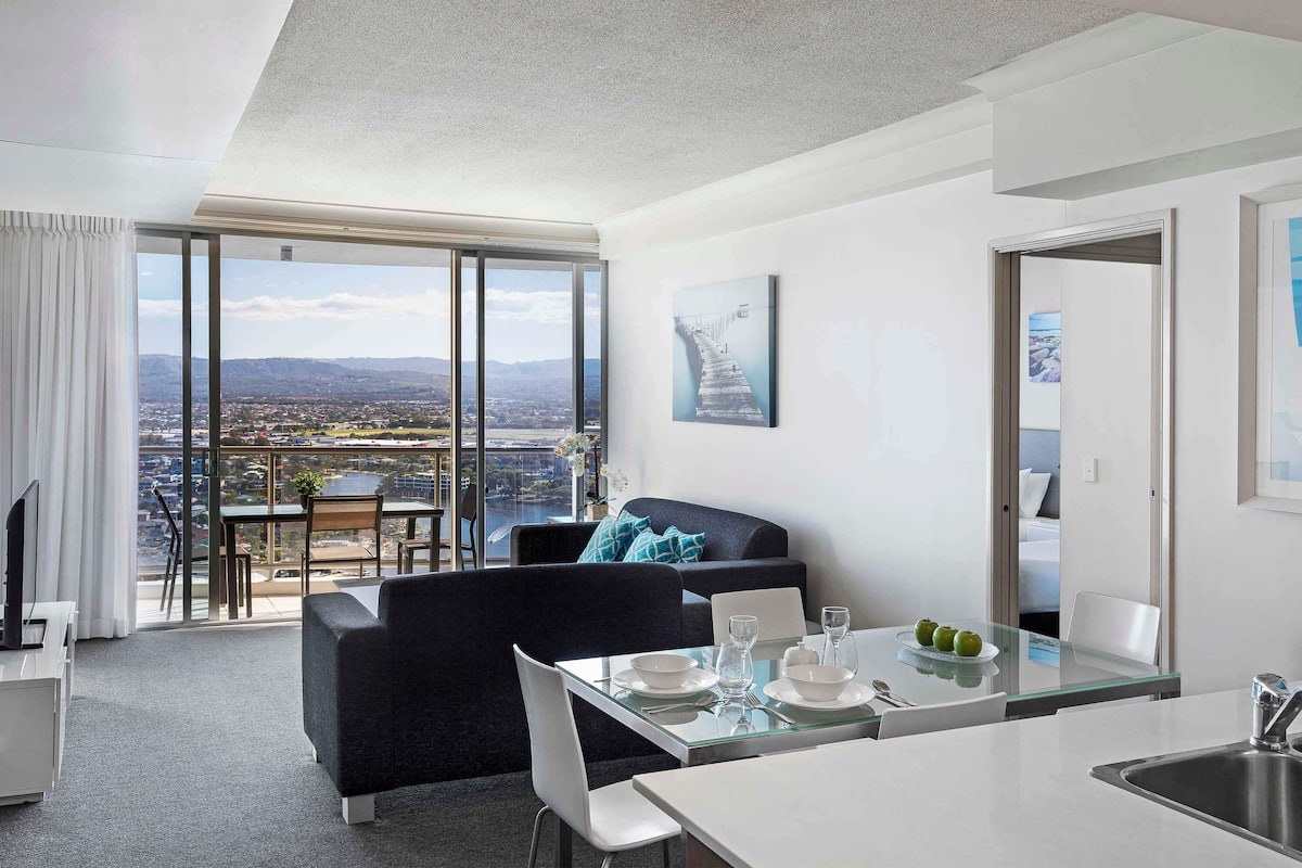A modern living room with a large window, a dining area, and a kitchen.