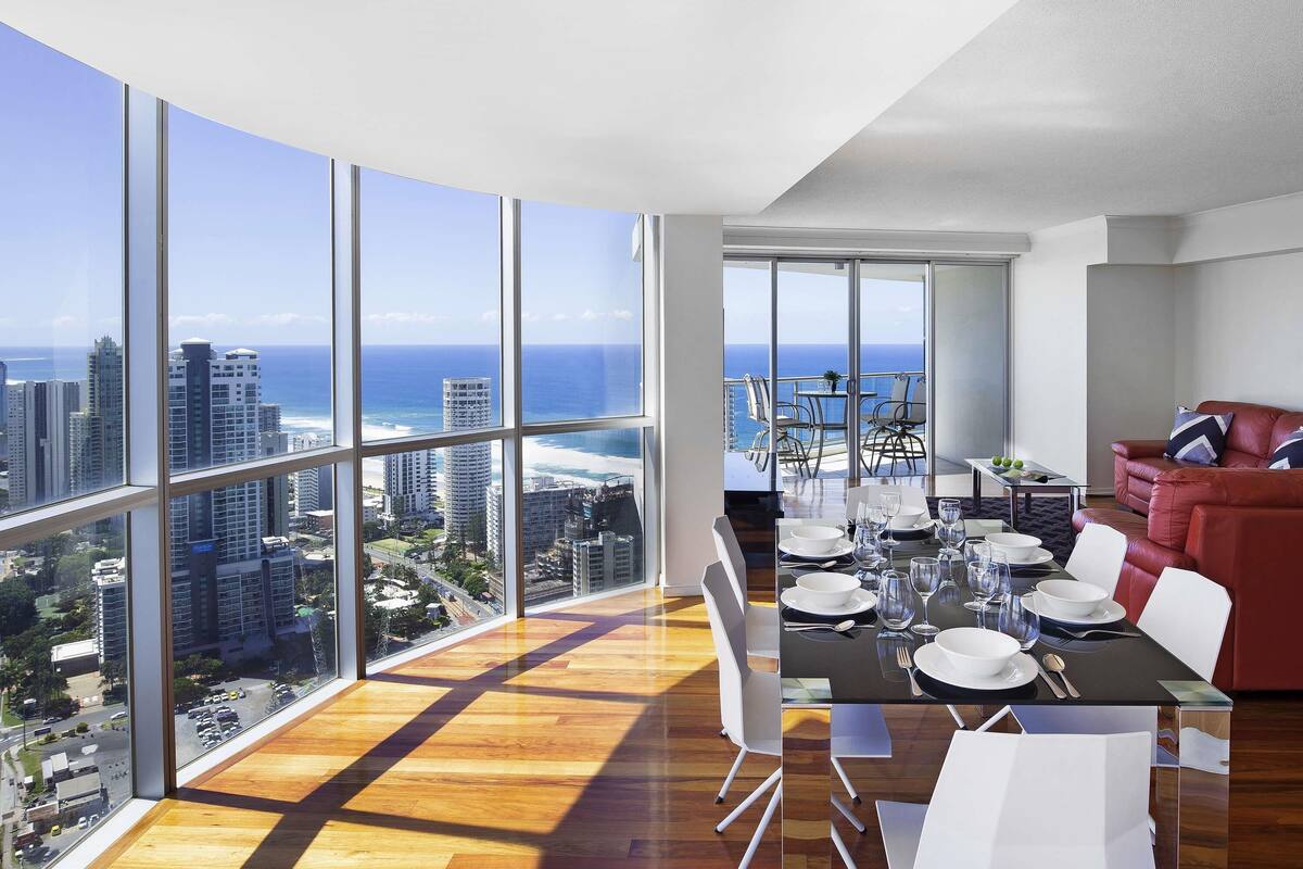 A high-rise apartment with a dining area, a red sofa, and a view of the city and ocean.
