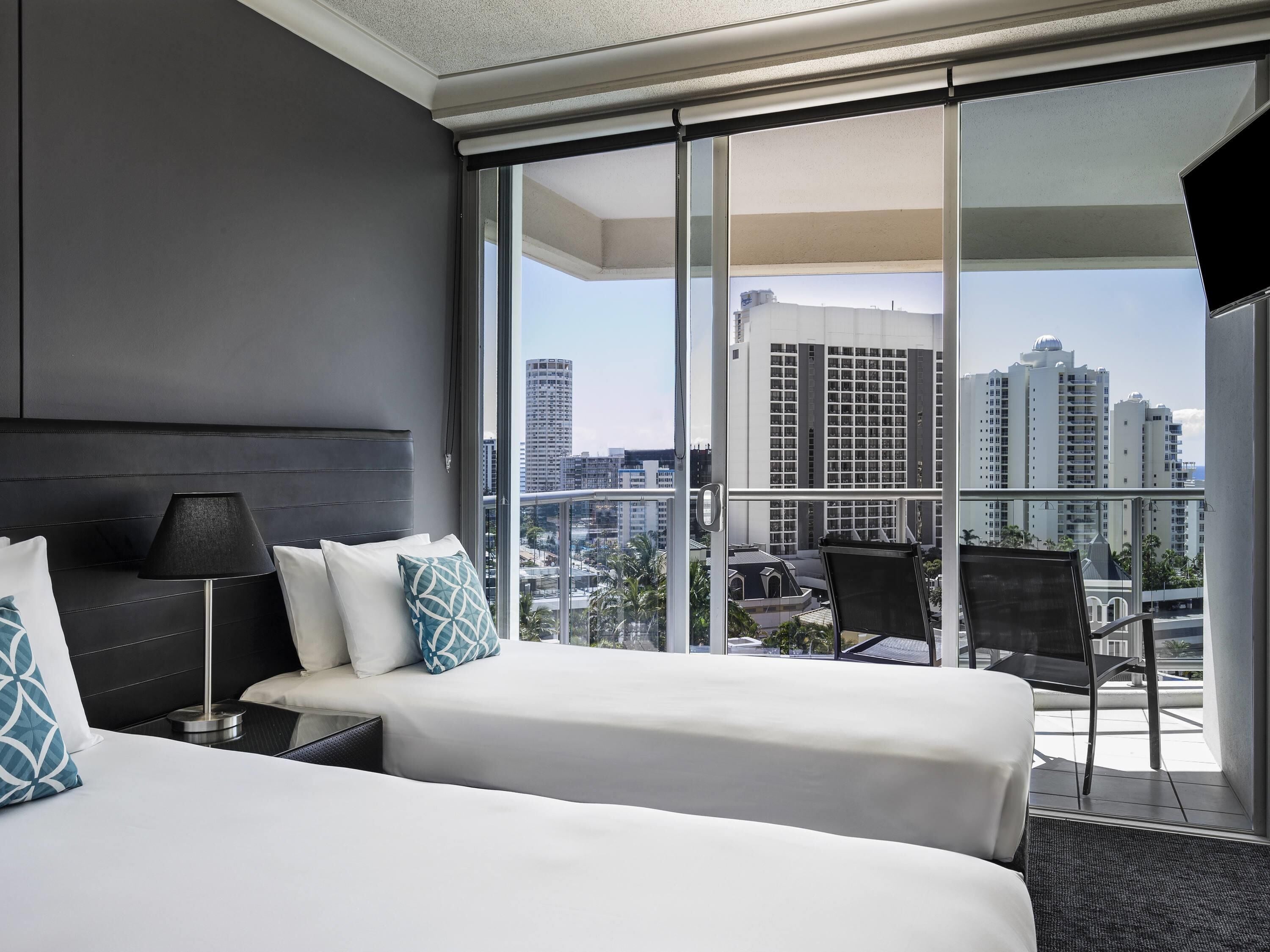 A hotel room with two beds, a large window, a chair, and a view of the cityscape.