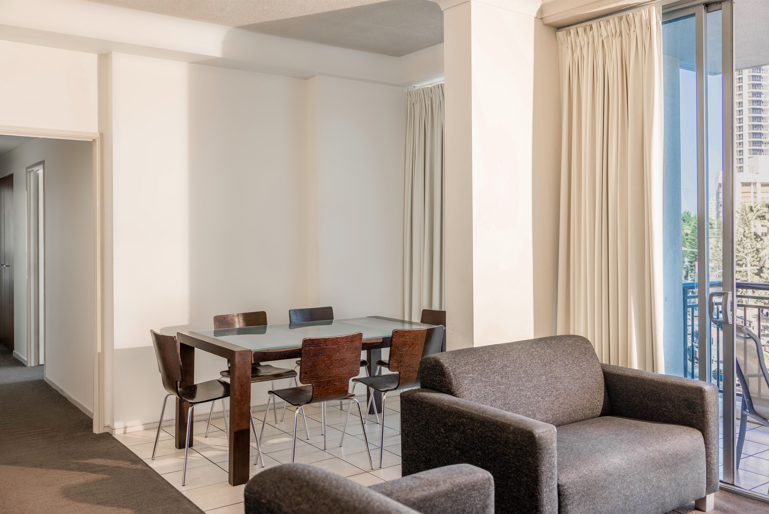 Une chambre d’hôtel moderne dotée d’un coin repas, d’un canapé et d’un balcon avec des rideaux.