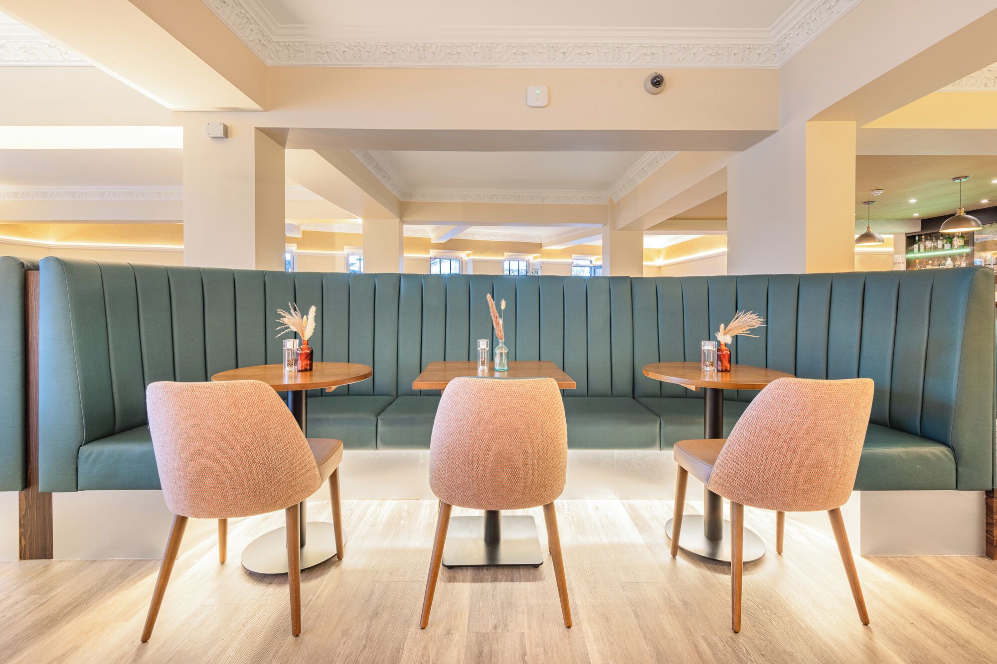 A restaurant with green booths, wooden tables, and woven chairs.