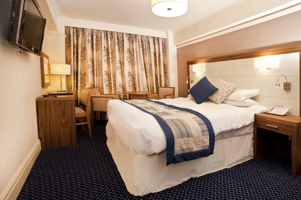 Una habitación de hotel con una cama grande, un escritorio con una silla, un televisor y una ventana con cortinas.