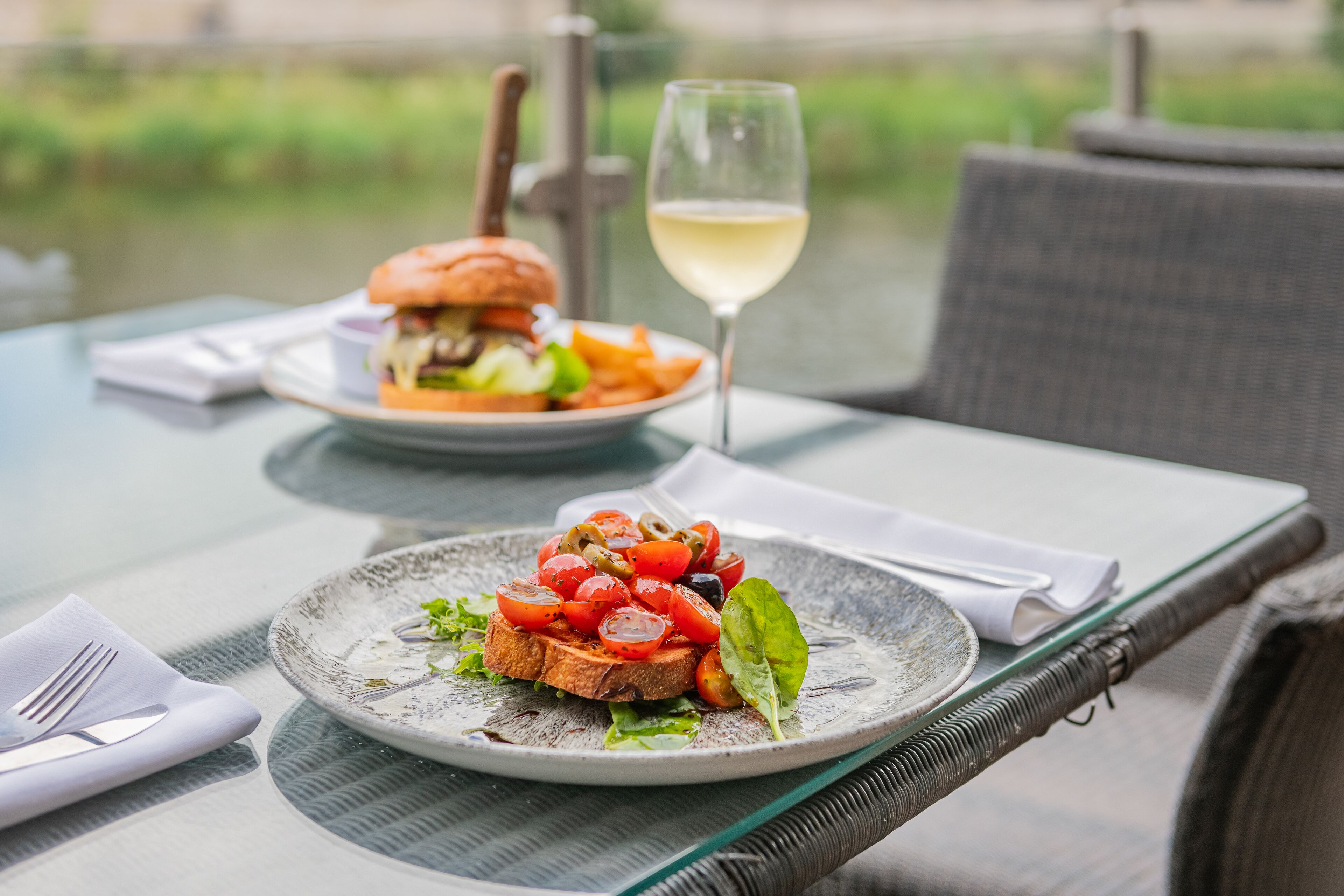 Una mesa con un plato de comida y una copa de vino blanco.