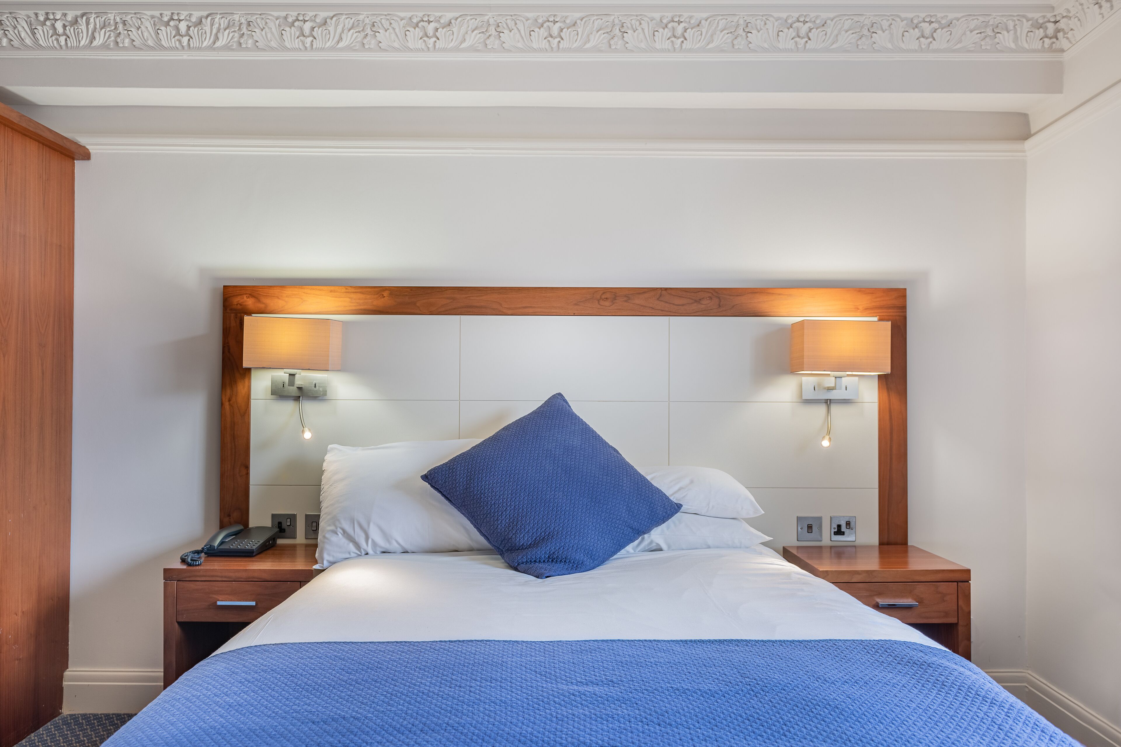 Un letto rifatto con un copriletto blu, due abat-jour e una testiera in legno.