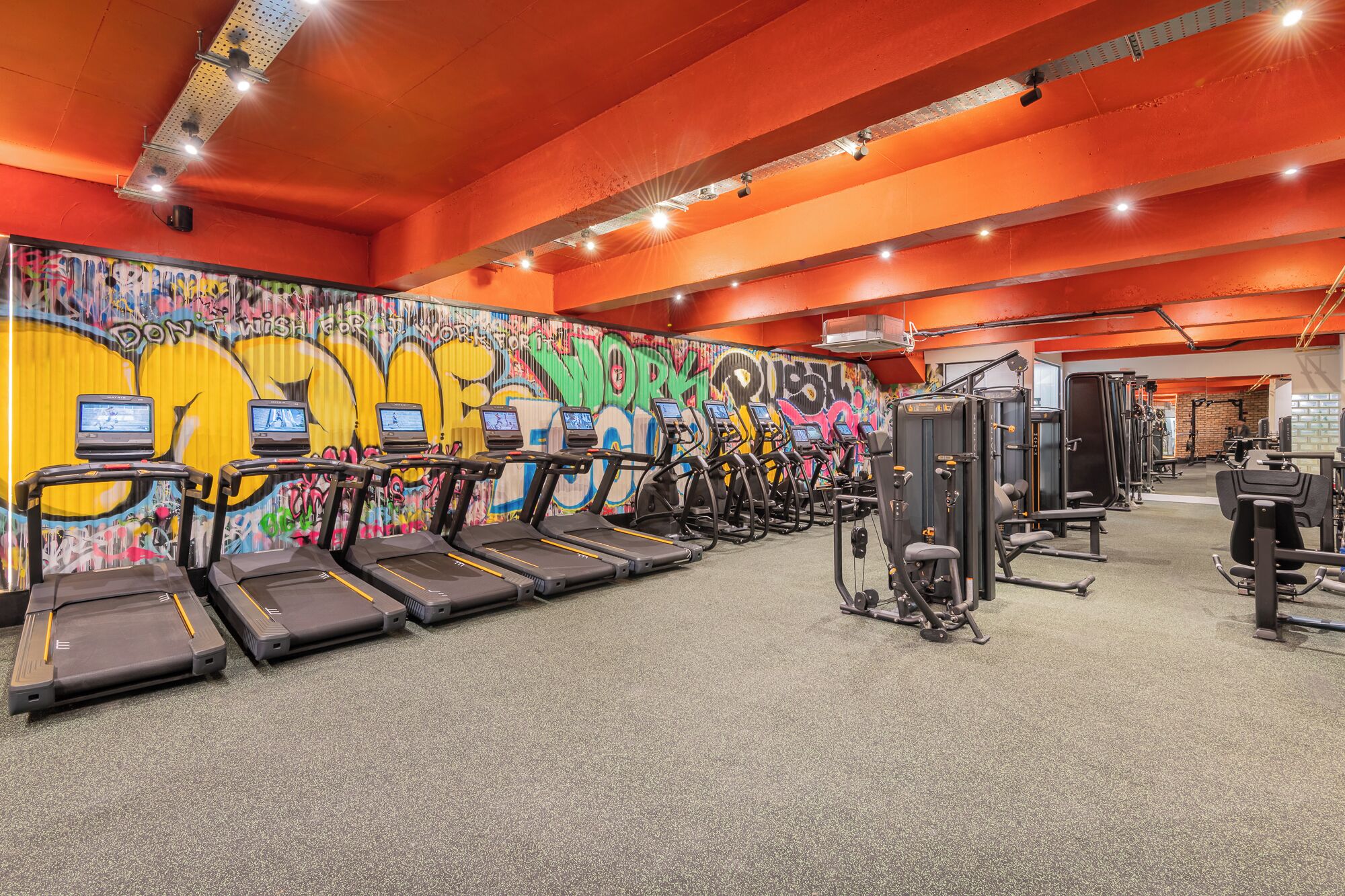 A gym with treadmills, weight machines, and a graffiti-covered wall.