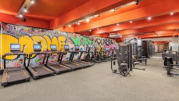 A gym with treadmills, weight machines, and a graffiti-covered wall.