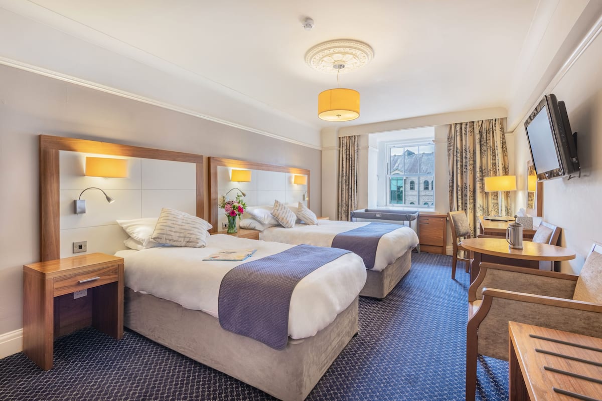 A hotel room with two beds, a desk, a chair, a TV, and a window with curtains.
