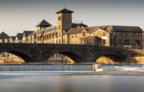 A stone bridge with three arches spanning a river, leading to a historic building with multiple windows and a tower.