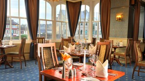 Comedor con mesas dispuestas para una comida, ventanas amplias y vistas de edificios.