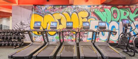 Ett gym med löpband, hantlar och en vägg täckt av graffiti.
