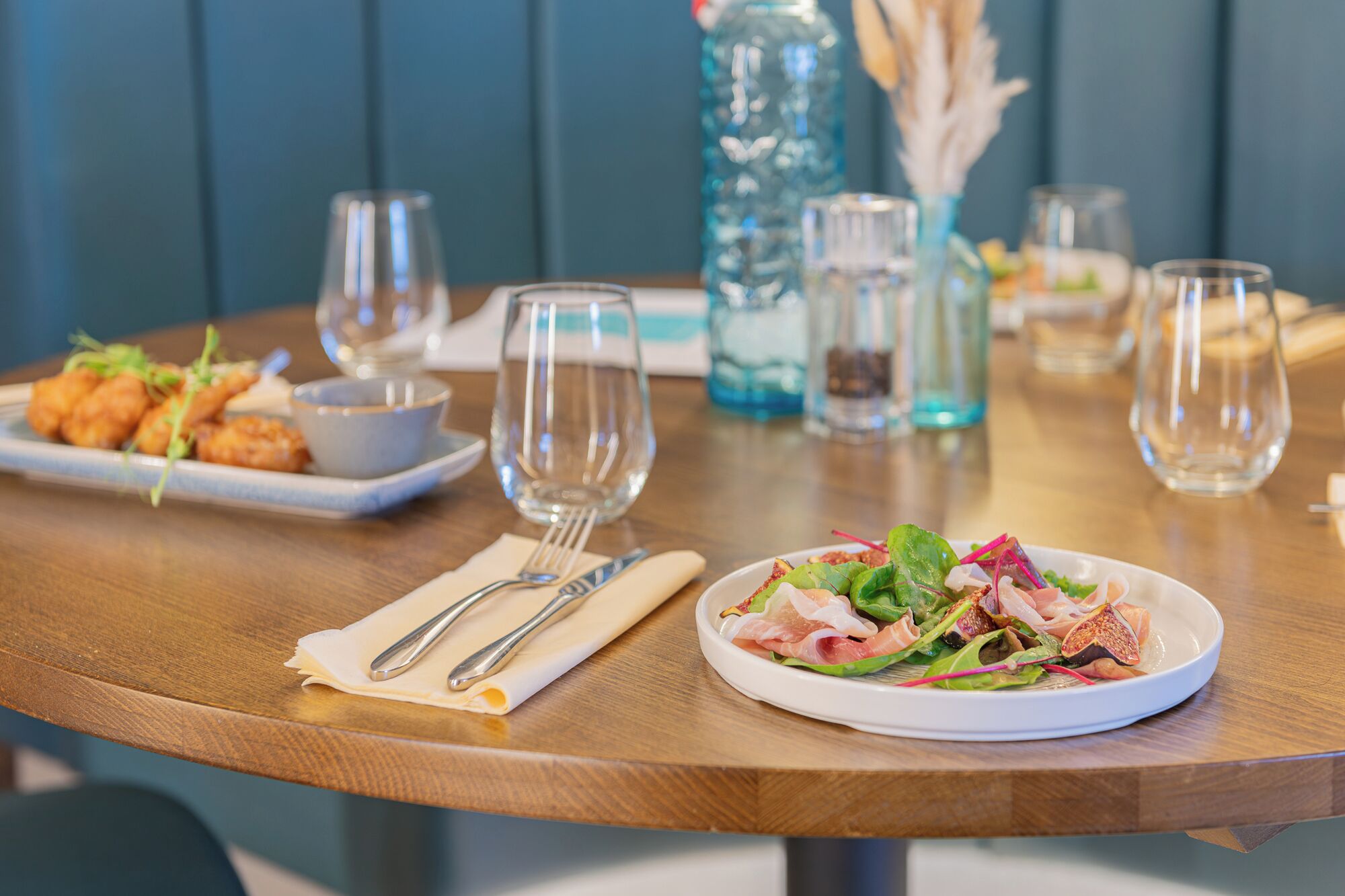A dining table with a plate of salad, a bowl of food, and empty wine glasses.
