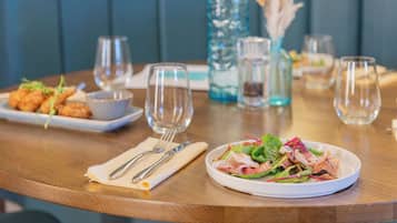 A dining table with a plate of salad, a bowl of food, and empty wine glasses.