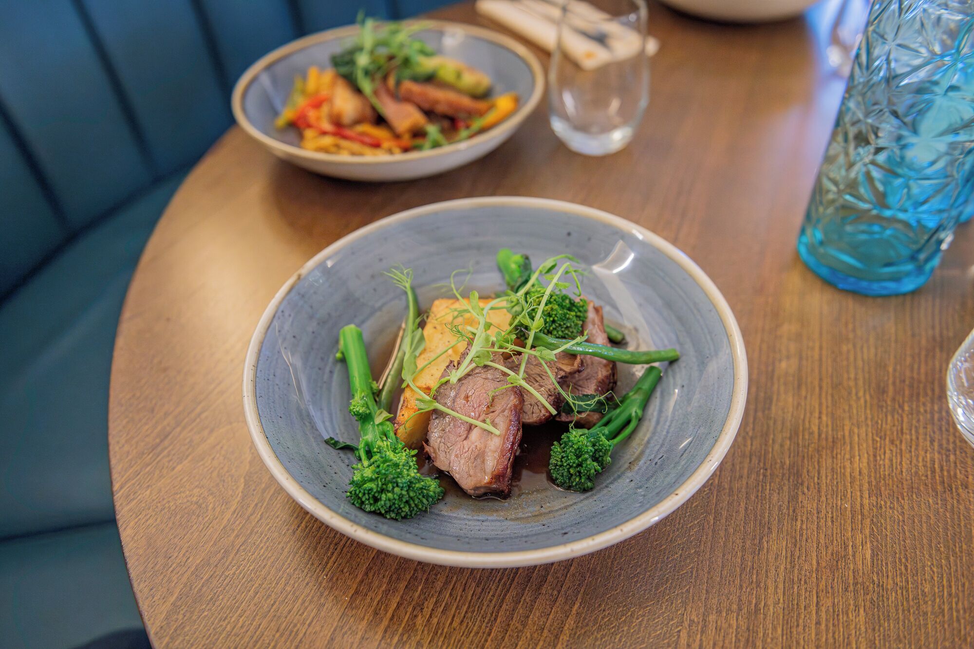 A dining table with a plate of food, a glass of water, and a blue glass container.