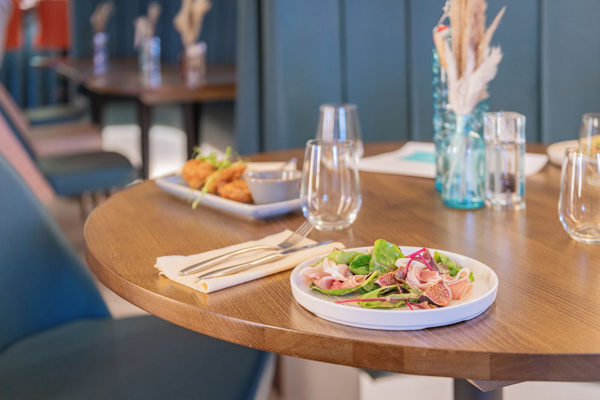A dining table with a plate of food, a glass of water, and a vase with dried plants.
