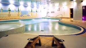 Una piscina interior con un diseño de cuadros en las paredes, un área de descanso con tumbonas y suelo de baldosas.