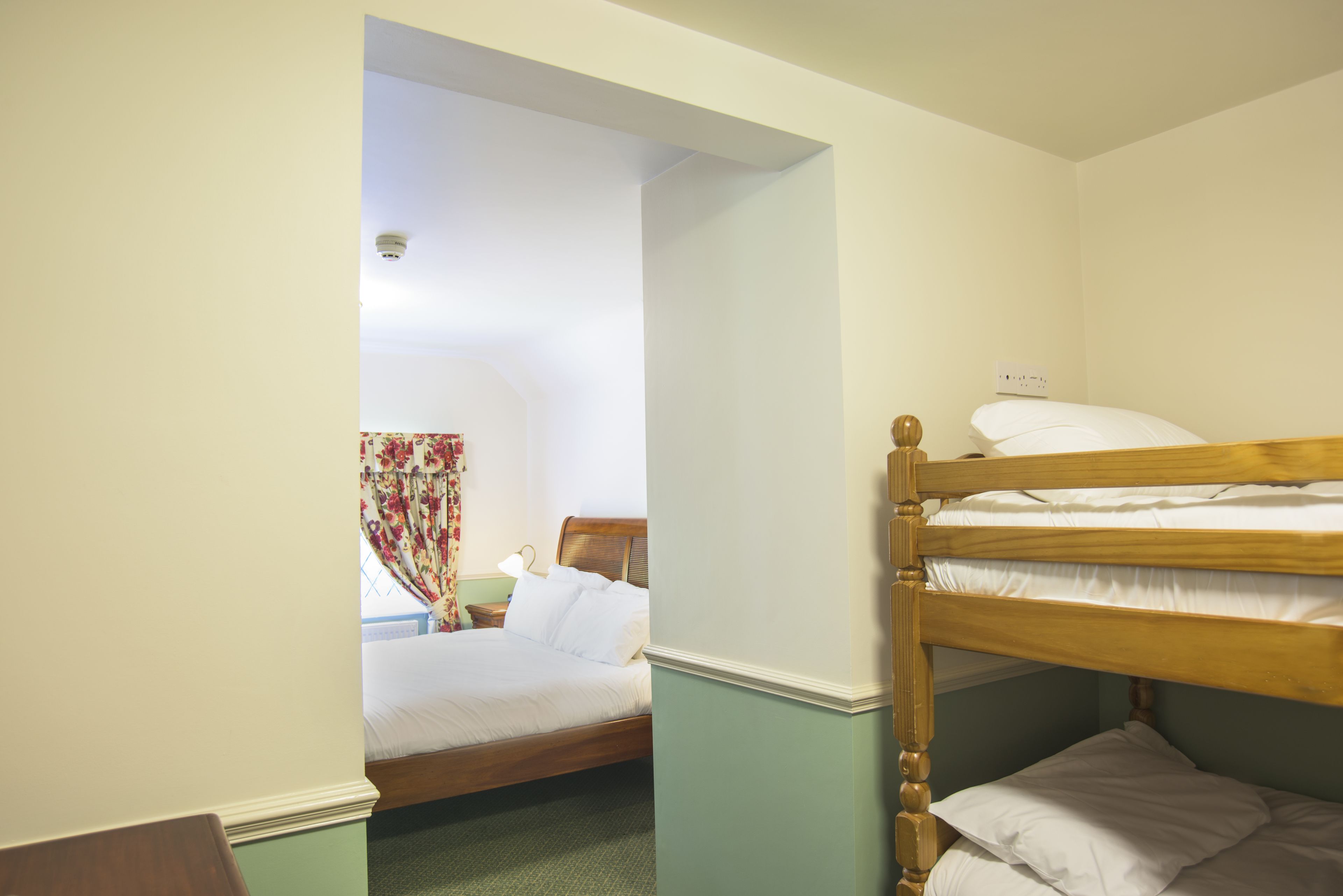 Ein Zimmer mit einem Etagenbett, einem Einzelbett und einem Fenster mit floralen Vorhängen.