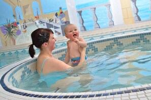 Une femme et un enfant dans une piscine, avec une fresque murale représentant une scène de plage.